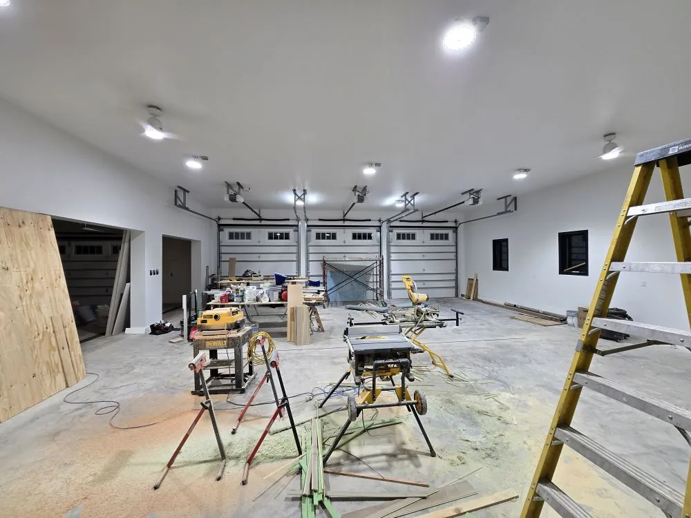 Vaulted shop interior during finish work, with three barn-style overhead doors.